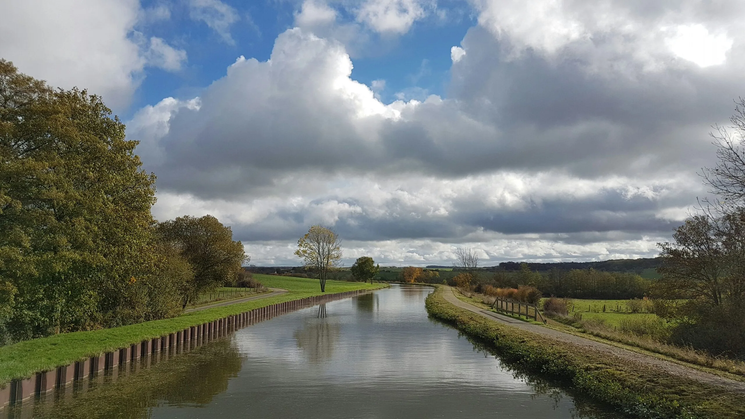 green grass field near river under white clouds and blue sky during daytime